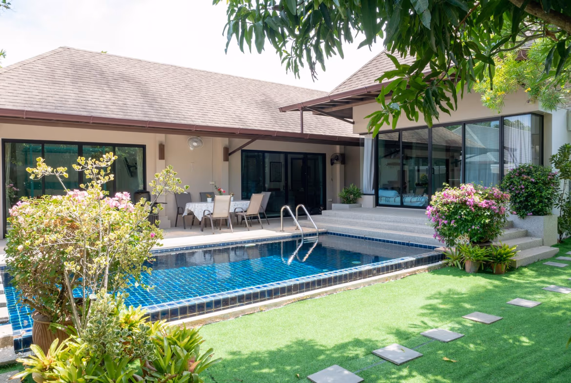 A bedroom with a wooden bed frame, white bedding, and a ceiling fan overlooks a private swimming pool.