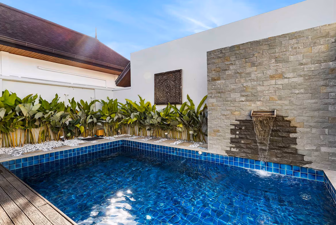 View of a swimming pool and patio with a hedge in the background.