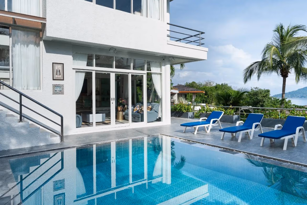 A white, modern five-bedroom villa in Patong with a private infinity pool overlooking the sea. The large patio features outdoor seating and lounges next to the pool.