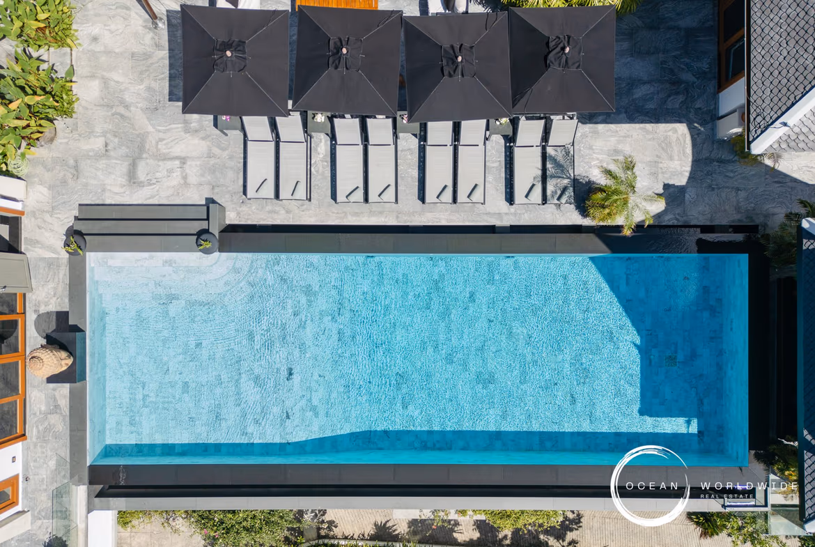 A spacious outdoor patio with lounge chairs looks out onto a swimming pool and the ocean.