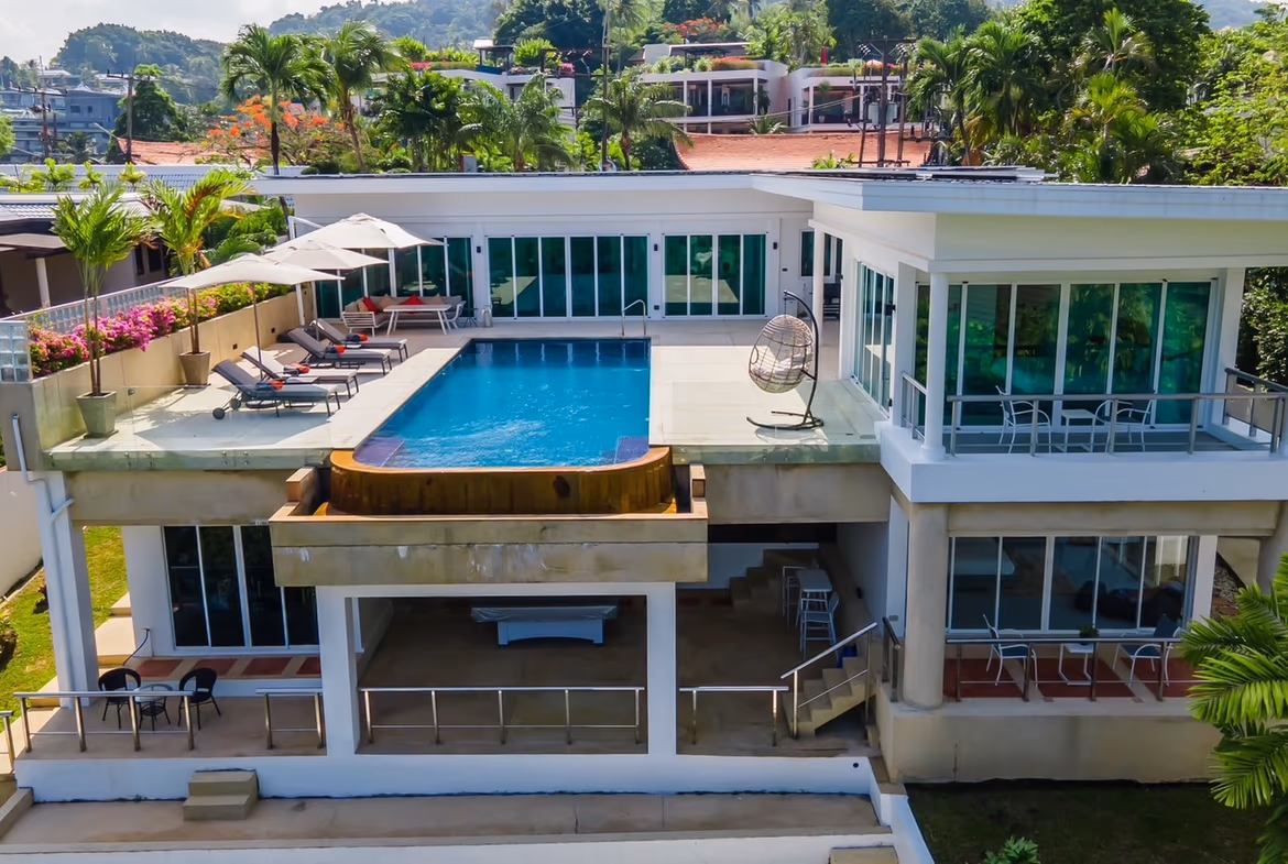 A three-bedroom villa in Kata features a long infinity pool overlooking the ocean. The multi-story home is built into a hillside and has several balconies.