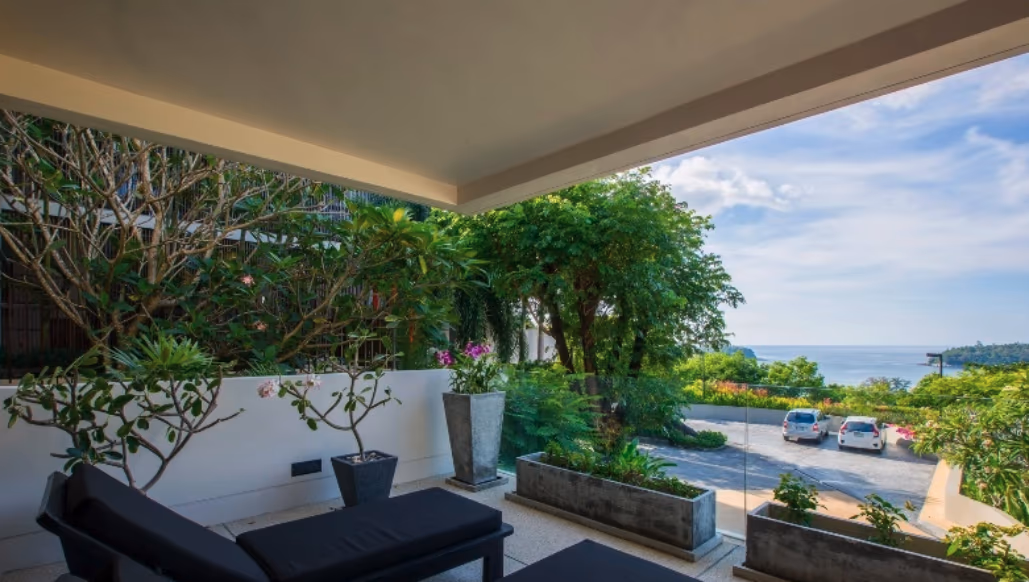 A partially covered balcony overlooks a swimming pool and the ocean.