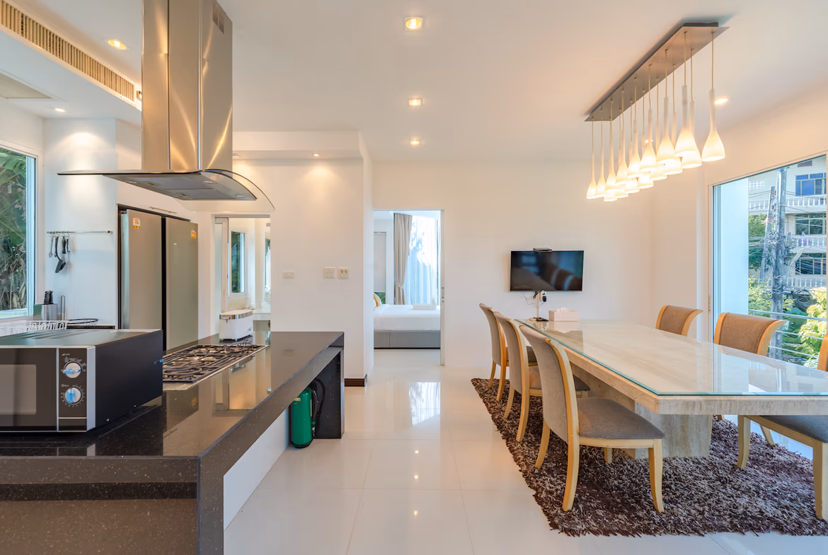 A spacious living area with white walls and a large, dark brown L-shaped sofa, facing a flat-screen TV mounted above a dark wood media console.