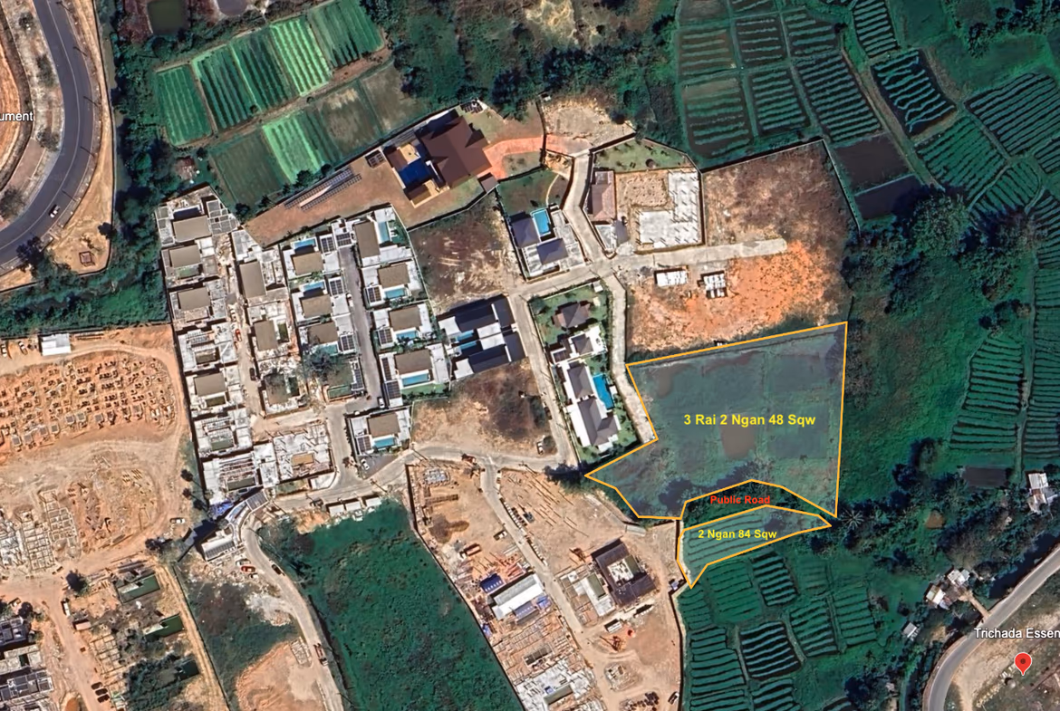 An aerial photo shows undeveloped land in Thalang. Trees and green vegetation cover the 4 Rai plot, neighboring properties, and a road.