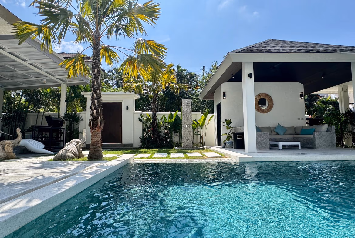 A spacious living room with modern furnishings and a view of the tropical garden and pool.