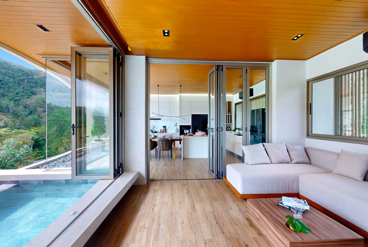 A spacious living room with a large L-shaped sofa and a view of a lush tropical garden.