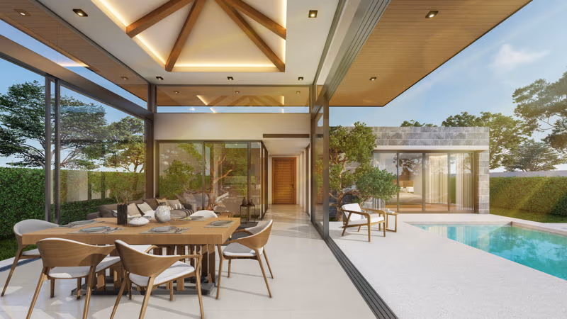 A spacious living room with modern furnishings and large windows showcasing an outdoor pool and tropical greenery.