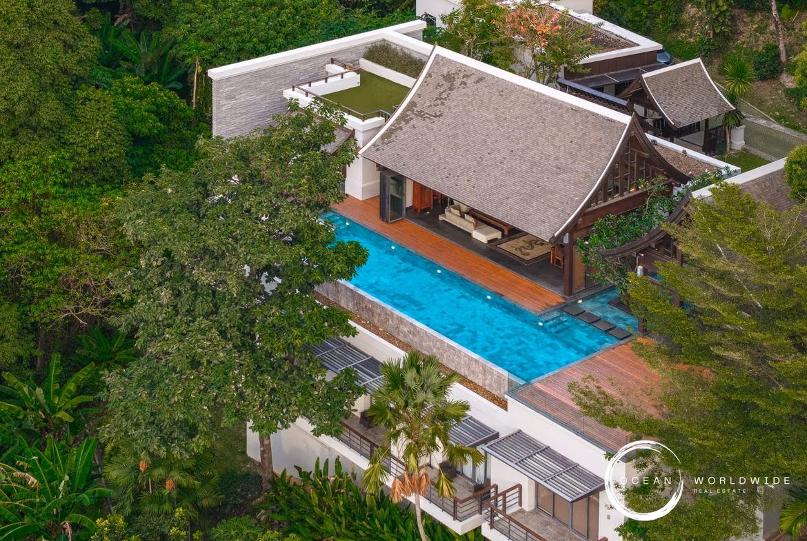 This image shows a bedroom with a large window overlooking a tropical forest and the ocean in the distance.