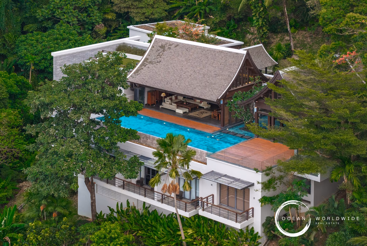 A serene bedroom with a canopy bed opens to a balcony overlooking a tropical forest and the ocean.