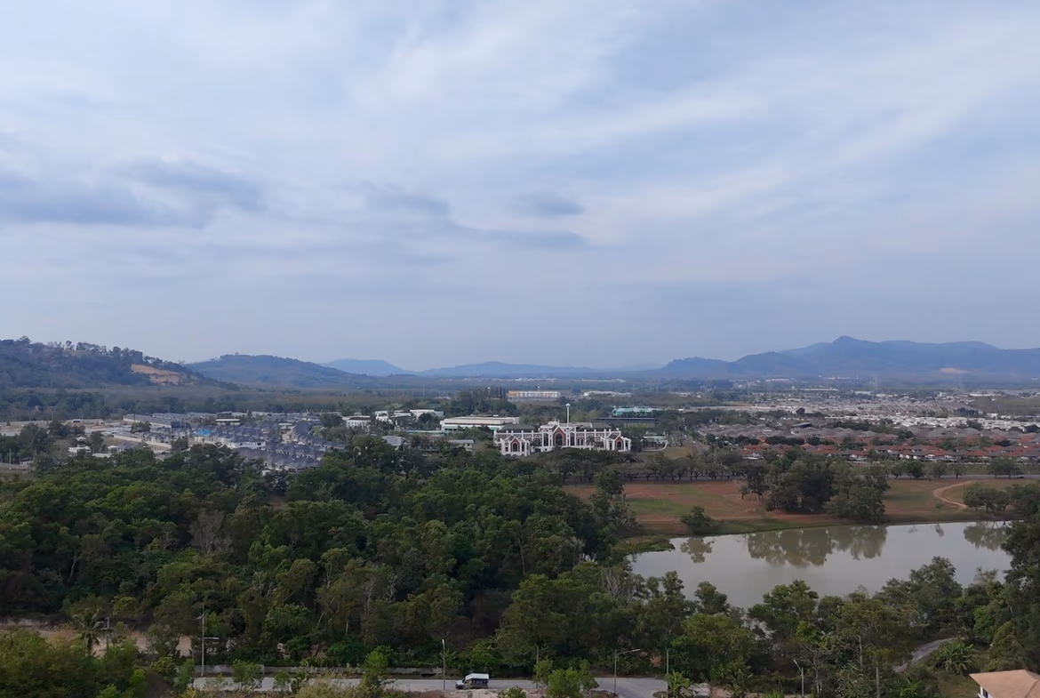 An elevated view of a land plot with distant mountains and a body of water under a partly cloudy sky.