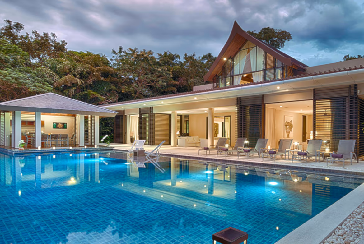 The photo shows an open-plan living area with an L-shaped sofa and a glass sliding door leading to an outdoor patio with a swimming pool.