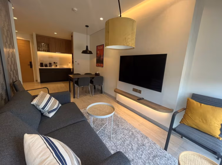 A modern living room with a sofa facing a television, brightly lit by natural light.