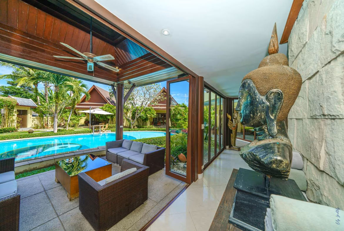 An aerial view shows the large villa property with multiple buildings and swimming pools nestled among lush greenery, with the ocean visible in the background.