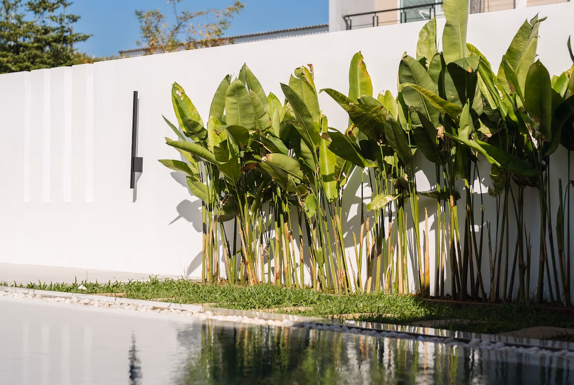 A brightly lit living room with modern furnishings opens onto a private swimming pool and garden area.