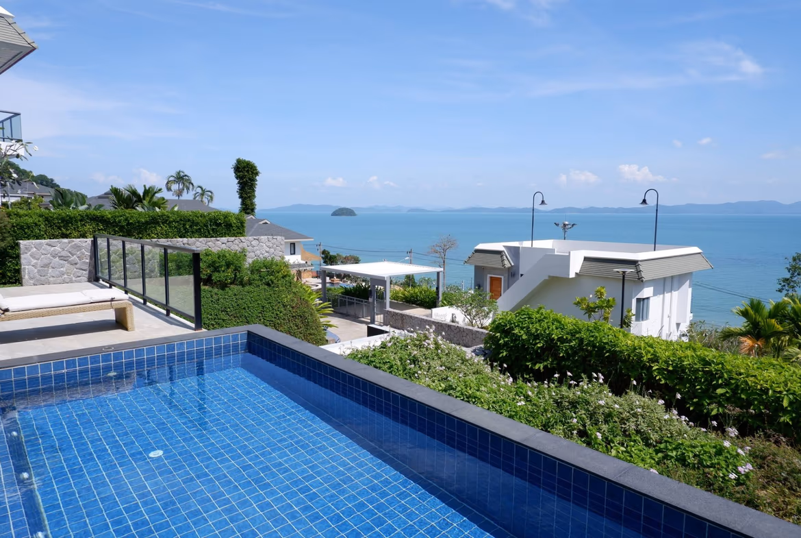 A white, three-bedroom villa in Cherngtalay, Thailand, features a balcony overlooking the sea and surrounding mountains.