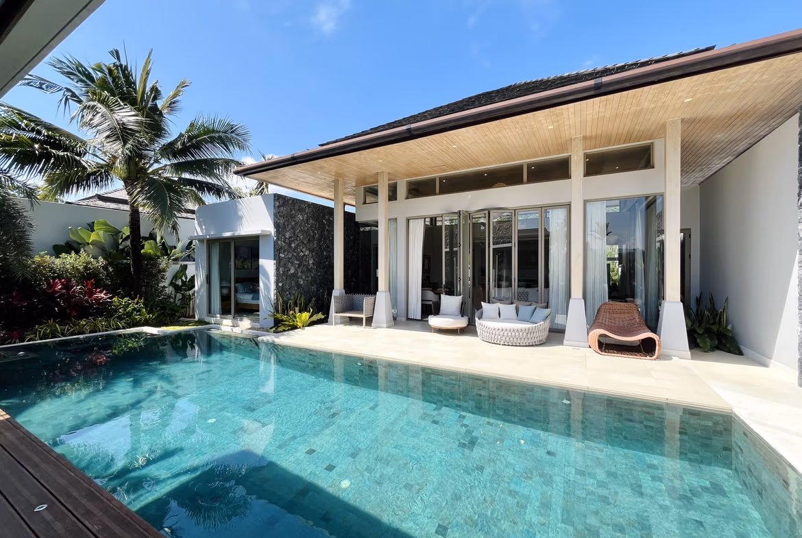 A 3-bedroom villa in Cherngtalay's gated community features a secluded pool surrounded by tropical plants. The single-story, white-walled home has a private patio area.