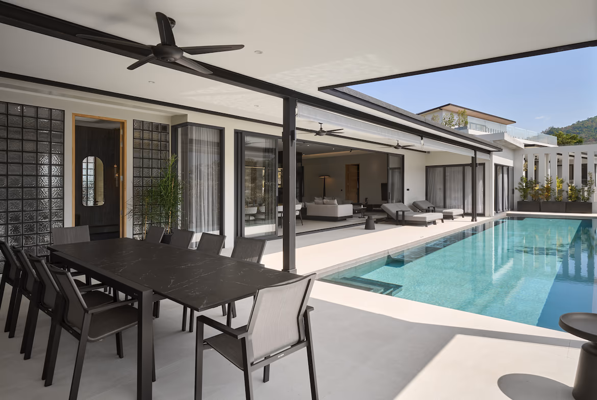 A spacious outdoor living area with a dark-tiled infinity pool overlooking a tropical landscape and mountains.