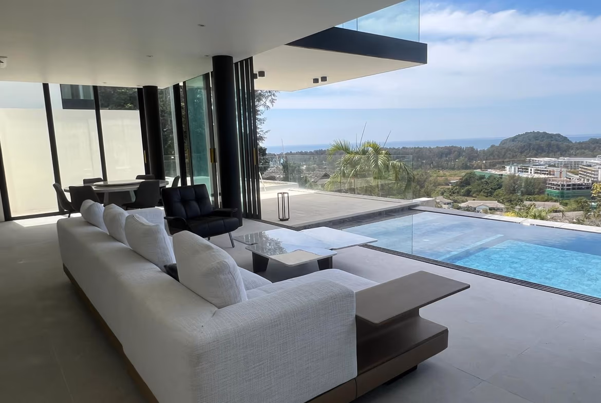 The photo shows an open-plan living area with modern furnishings and a sea view through large glass doors.