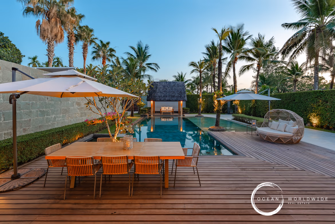 A spacious living room with large windows overlooking a swimming pool and tropical landscaping.