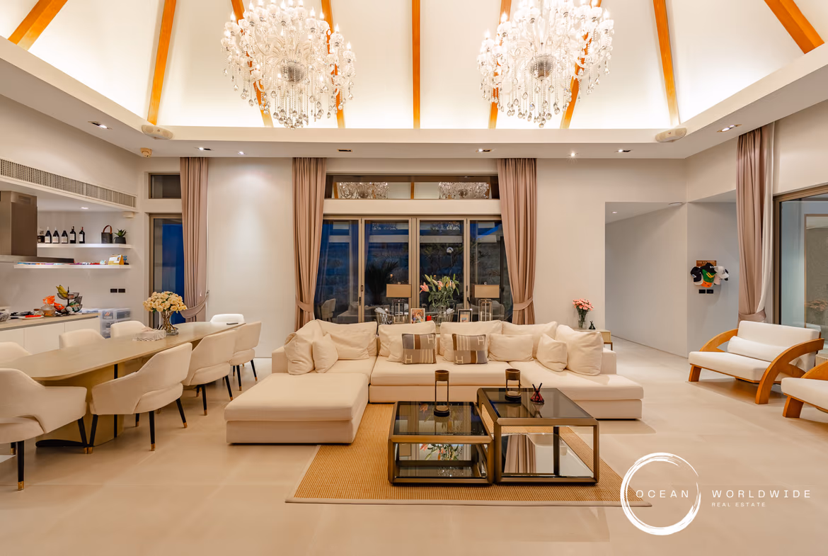 A spacious open-concept living area with modern furnishings and large windows overlooking a pool and garden.