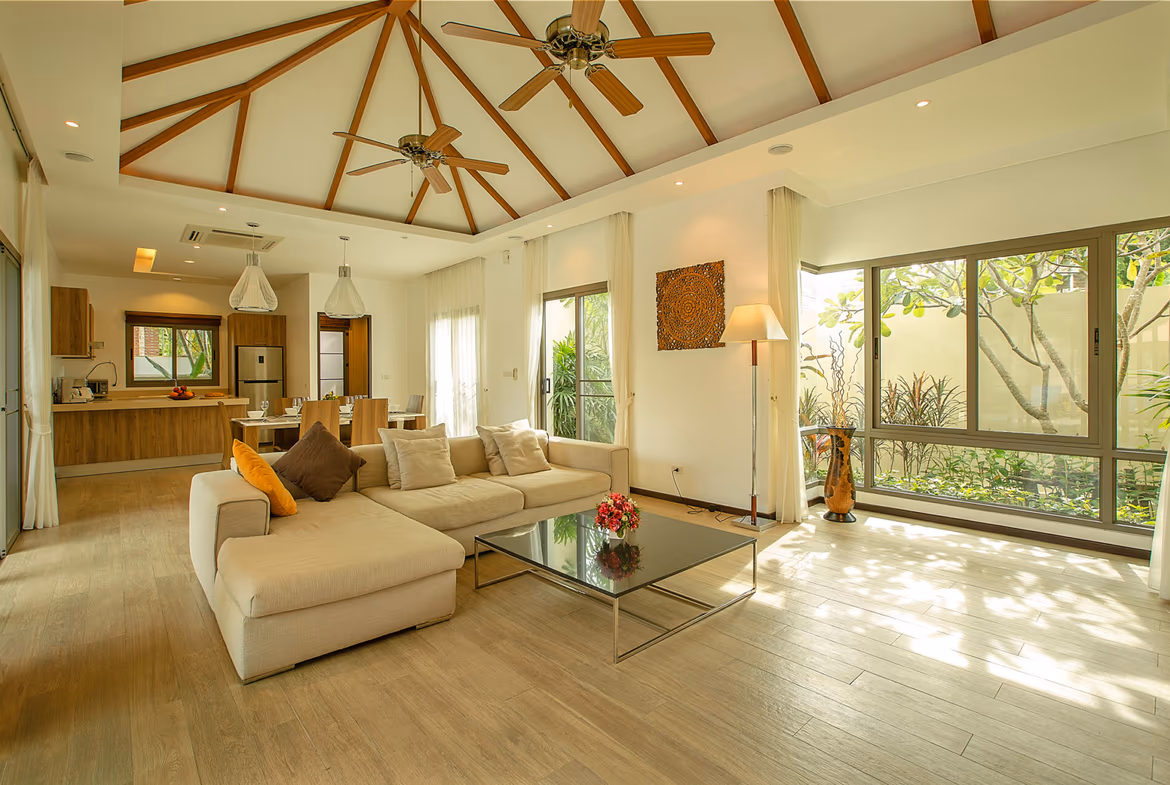 A living room with a sofa and an open patio door leading to a swimming pool.