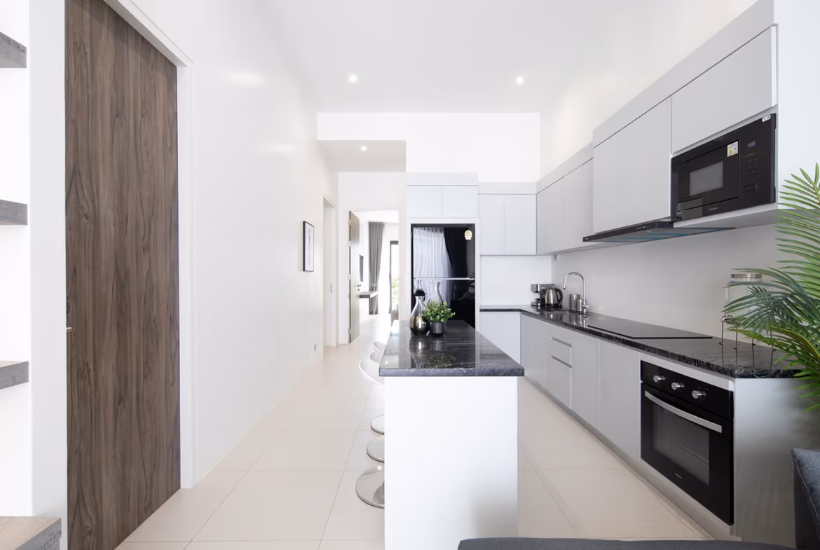 Bright modern kitchen with white walls, grey cabinets, black countertops, and stainless-steel appliances along a long counter.
