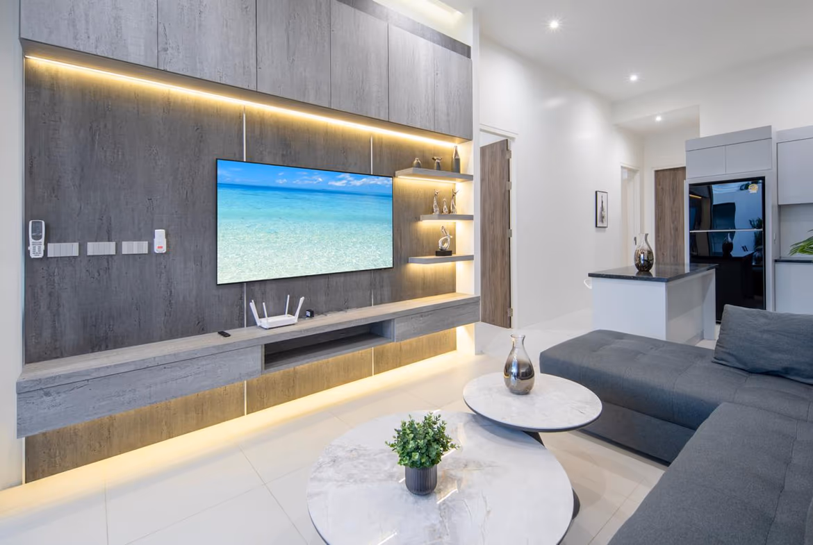 Contemporary living room with a wall-mounted TV on gray wood paneling, illuminated shelves, and a gray sectional sofa.