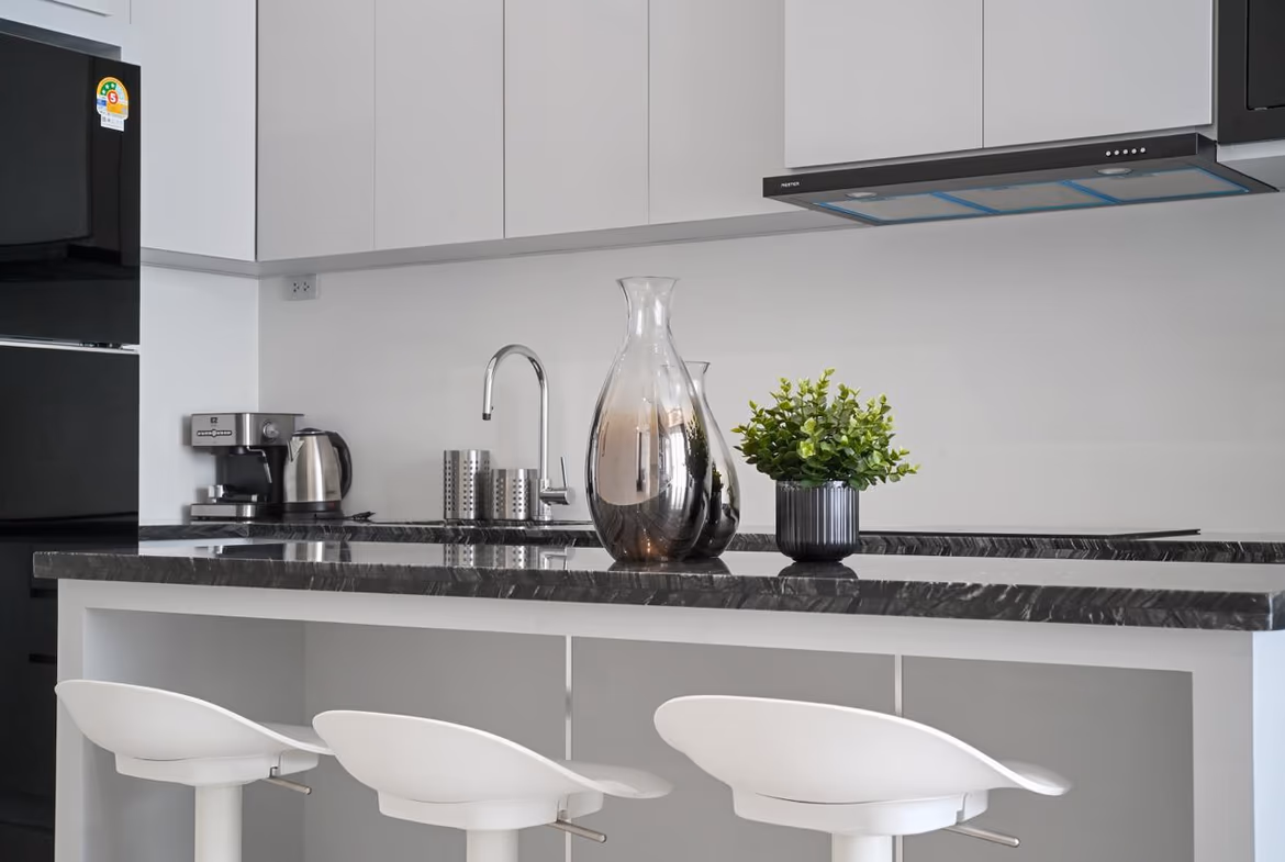 Modern kitchen island with a black marble countertop, three white bar stools, and a glass carafe center stage.