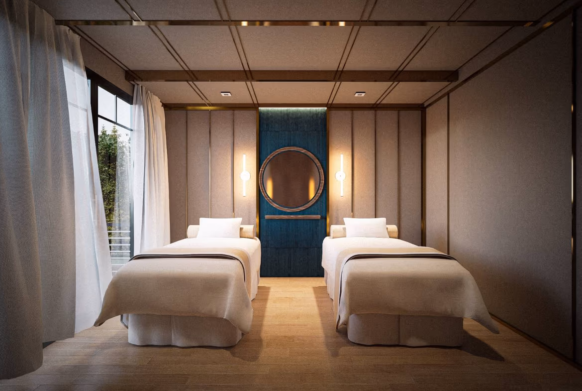 Twin hotel room with two single beds, beige bedding, and a blue paneled wall featuring a round mirror between warm wall lamps on either side.
