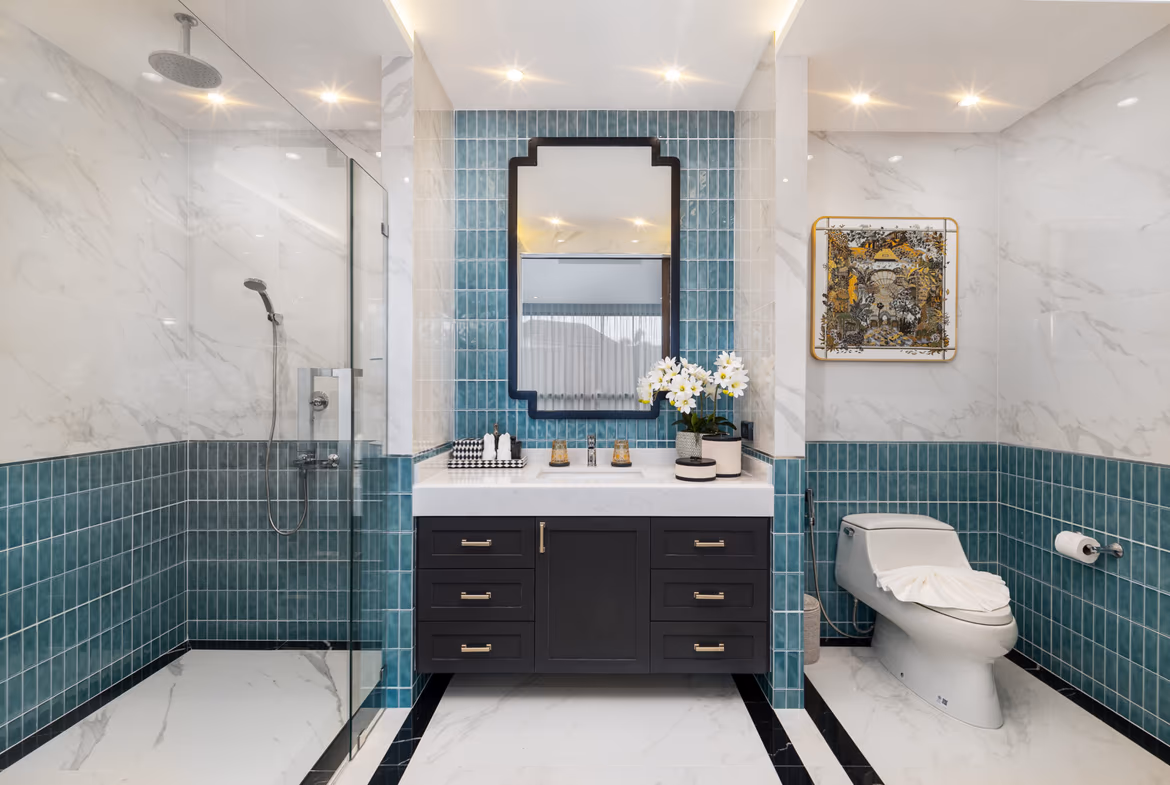 Luxurious bathroom with teal tile accents, a black double-drawer vanity, and a mirror above a marble countertop with white flowers and accessories.
