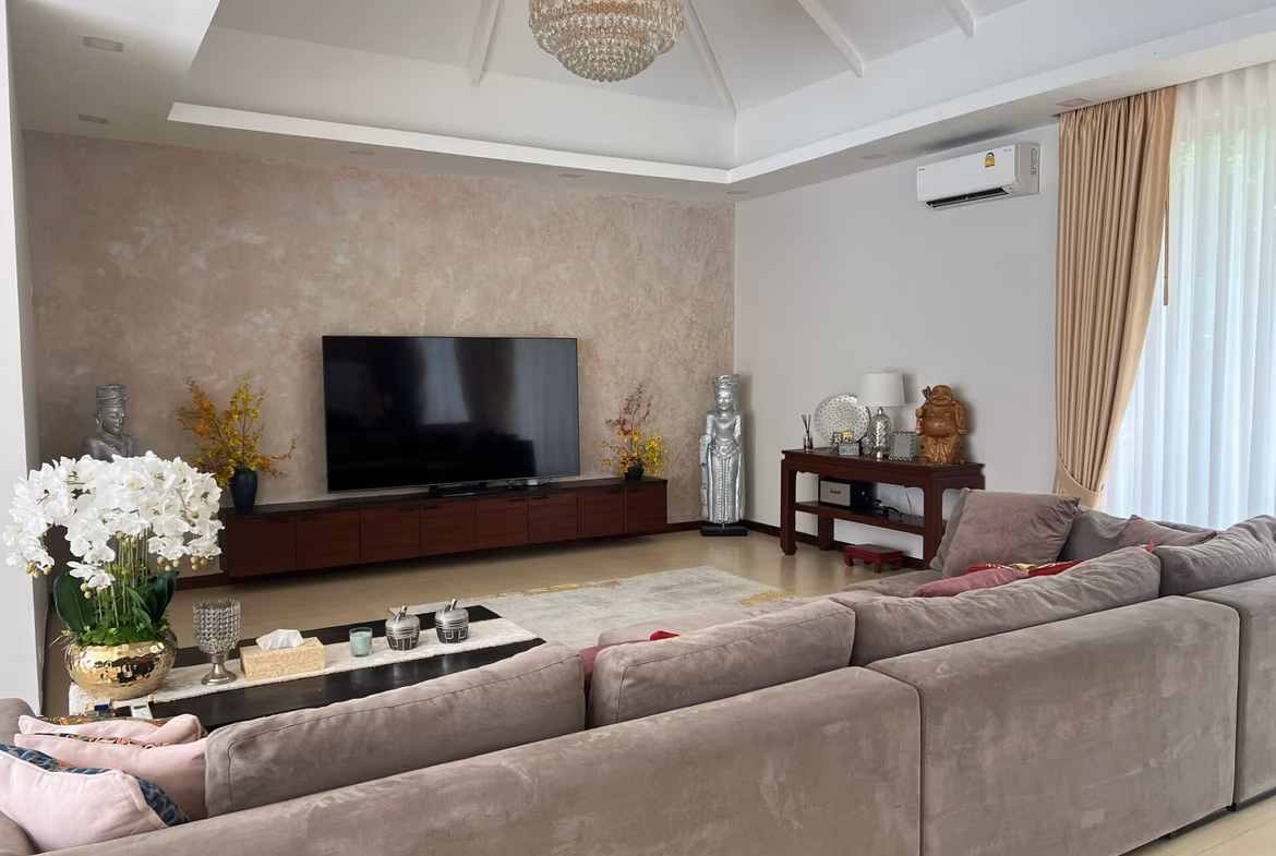 Living room with a large gray sectional sofa facing a wall-mounted flat-screen TV, beige accent wall, and a chandelier overhead.