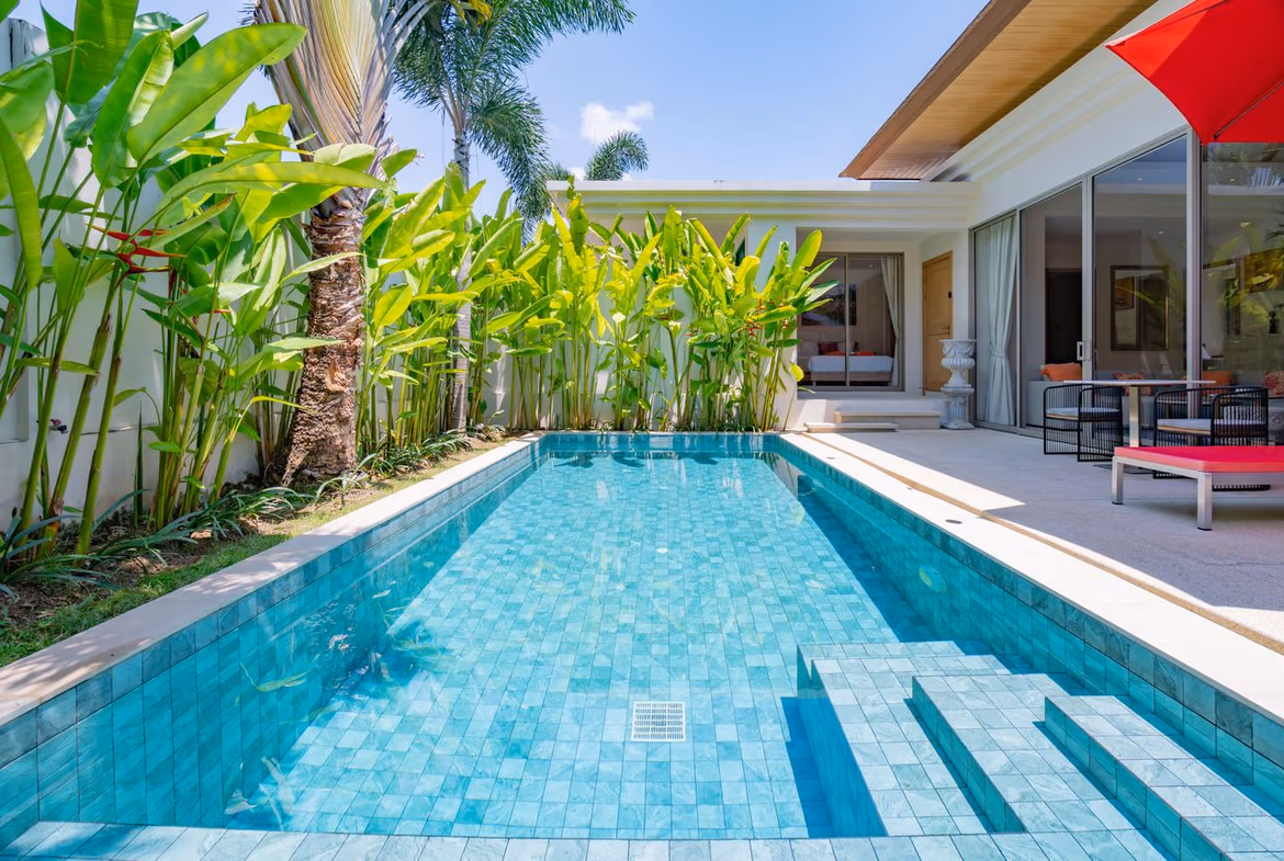 Luxurious backyard with a turquoise tiled pool, palm plants along a white wall, and a modern patio with seating and a red umbrella.
