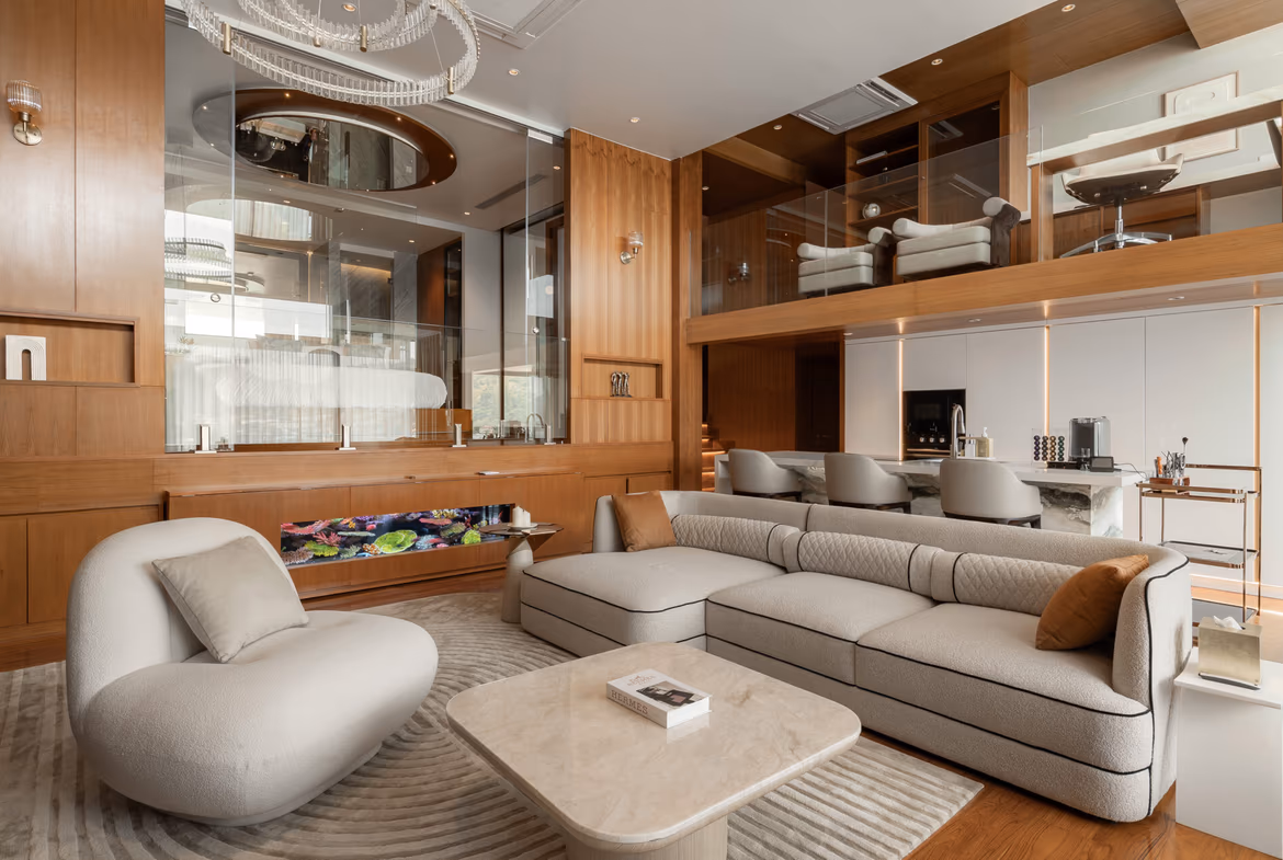 Luxurious open-plan living area with cream sectional sofa, marble coffee table, and warm wood paneling; glass mezzanine in background.
