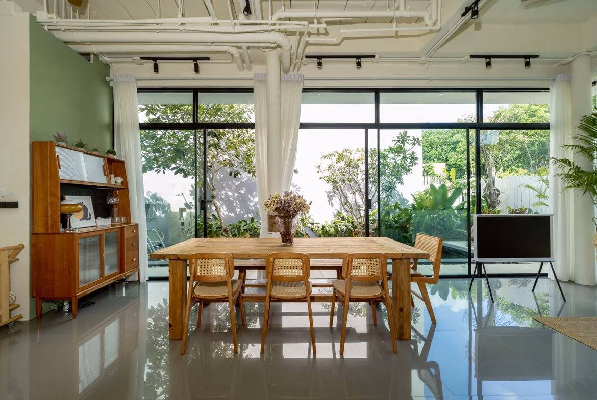 Open-plan dining room with a wooden table and chairs, large glass doors showing a lush garden outside.