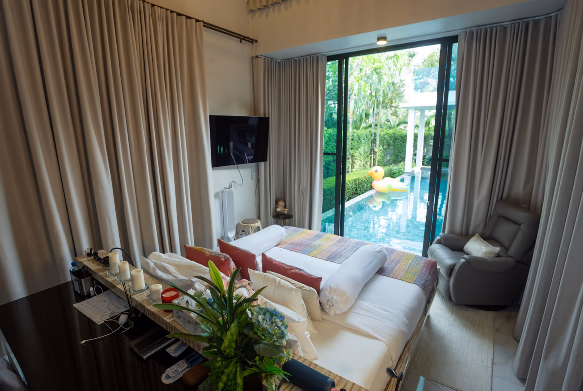 Bedroom with a view: bed facing sliding glass doors to a pool area and a rubber duck float outside, beige curtains on sides.