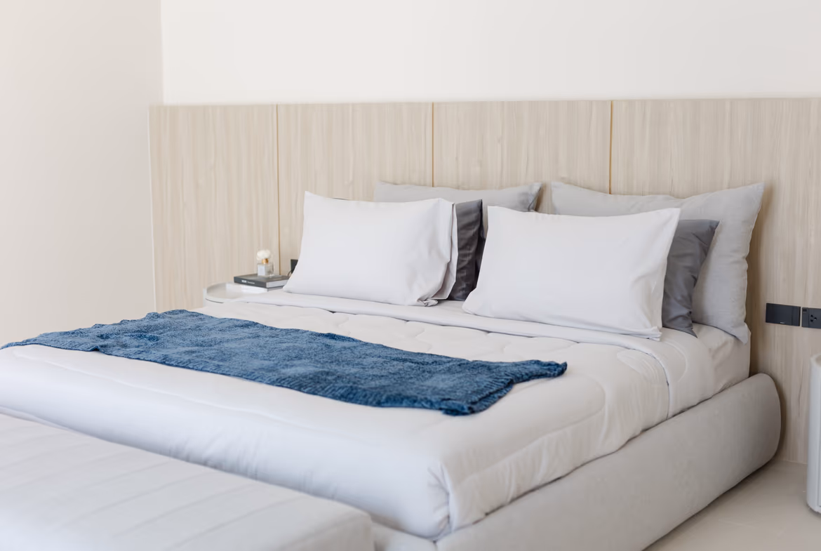 Hotel-style bedroom with a large bed, white linens, gray and white pillows, and a blue throw across the foot of the bed.