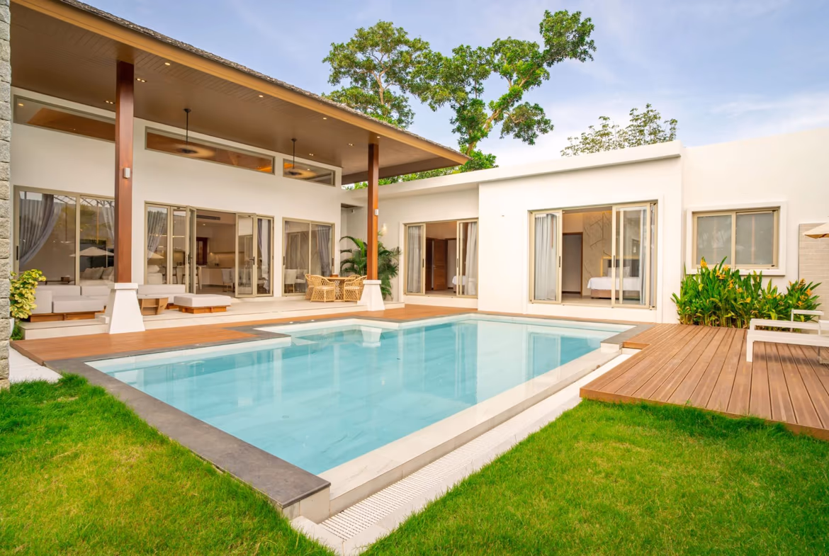 Modern white villa with a rectangular pool, wooden deck, and open living spaces by glass doors right outside the home.