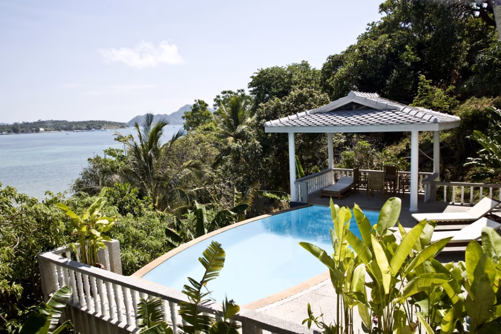 Infinity pool with a tropical garden and an ocean view, plus a shaded gazebo and lounge seating nearby.