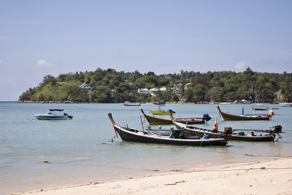 Small boats anchored near a sandy beach with a forested island in the background.