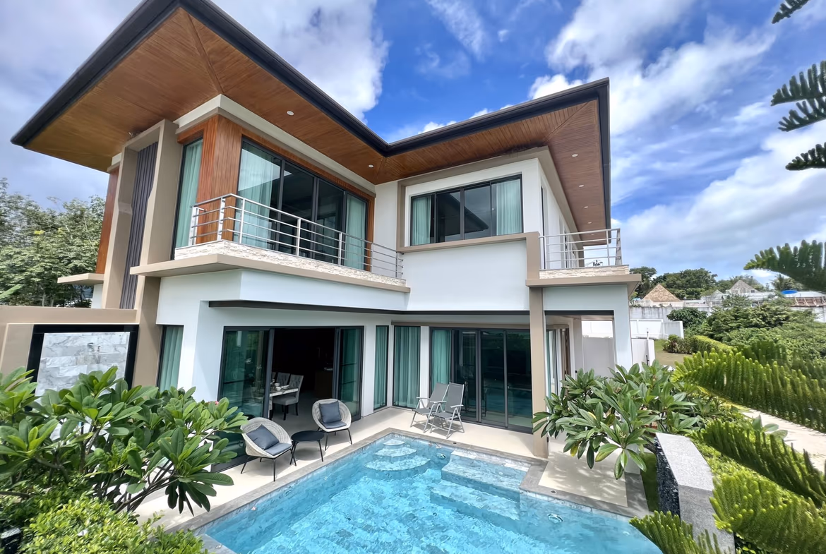 Modern two-story house with wooden overhangs, glass doors, and a rectangular pool in the courtyard, under a bright sky.