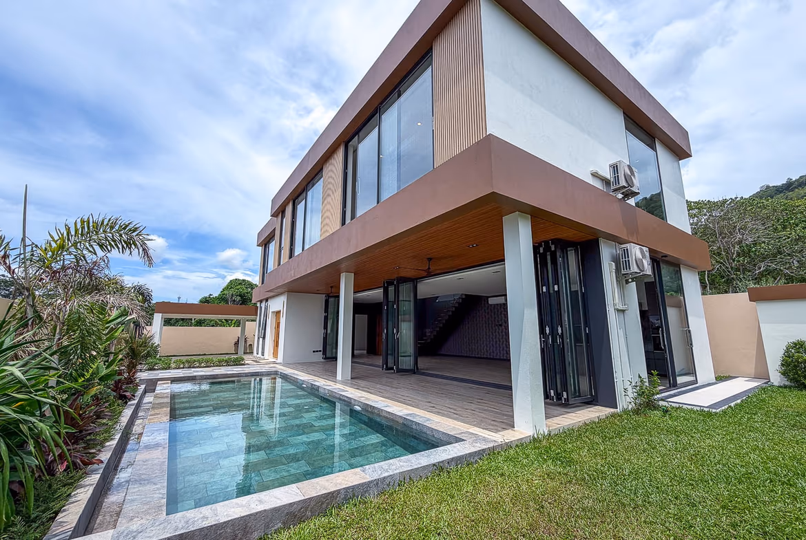 Contemporary two-story house with large glass windows and a rectangular in-ground pool in the backyard under a blue sky.