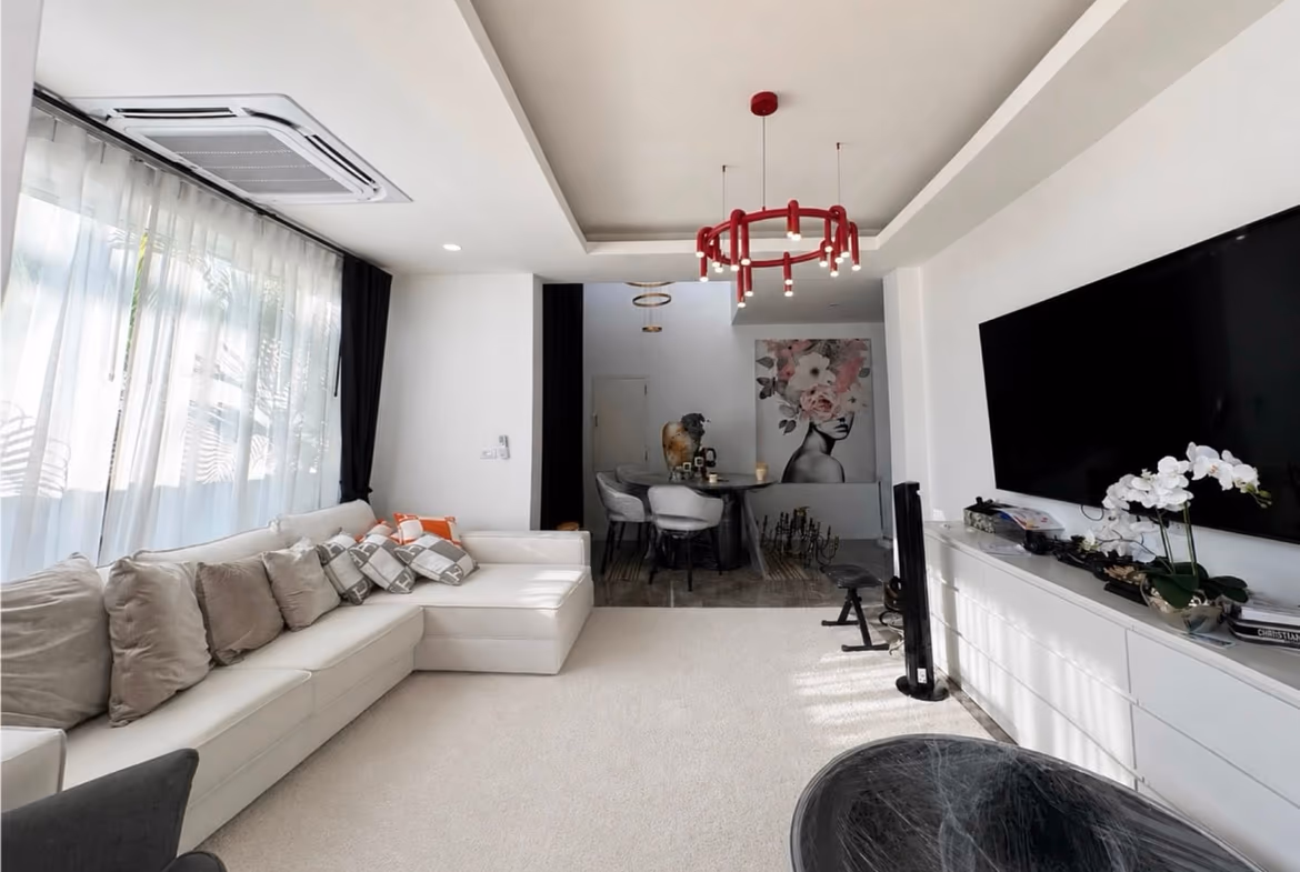 Bright modern living room with a white sectional sofa, sheer curtains, and a red circular chandelier hanging from a recessed ceiling.