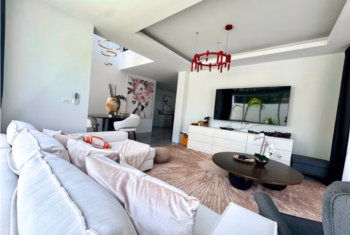 Modern living room with a white sectional, wall-mounted TV on a white media console, round coffee table, and a red chandelier overhead.